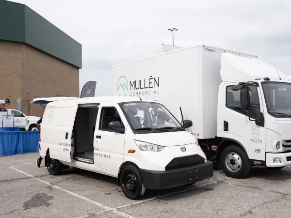 A Mullen One cargo van sits next to a Mullen Three low cab forward truck on display.
