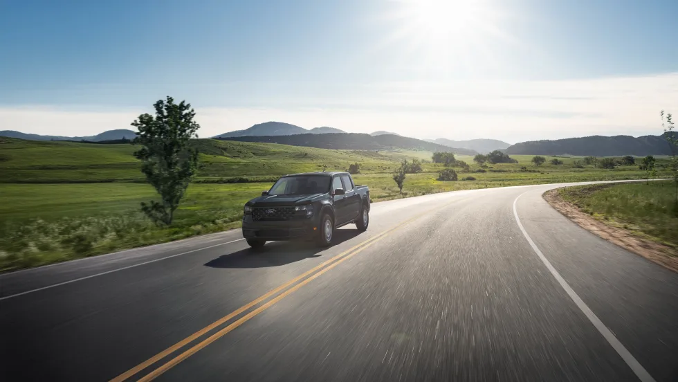 A black Ford Maverick XL is shown driving down a rural road.