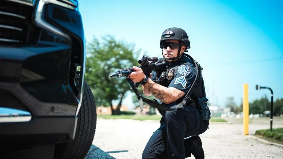 Police officer crouching behind vehicle, holding rifle in tactical stance