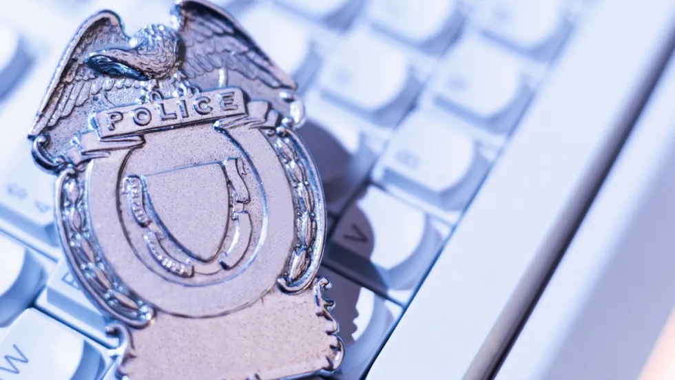 Silver police badge with eagle emblem resting on computer keyboard