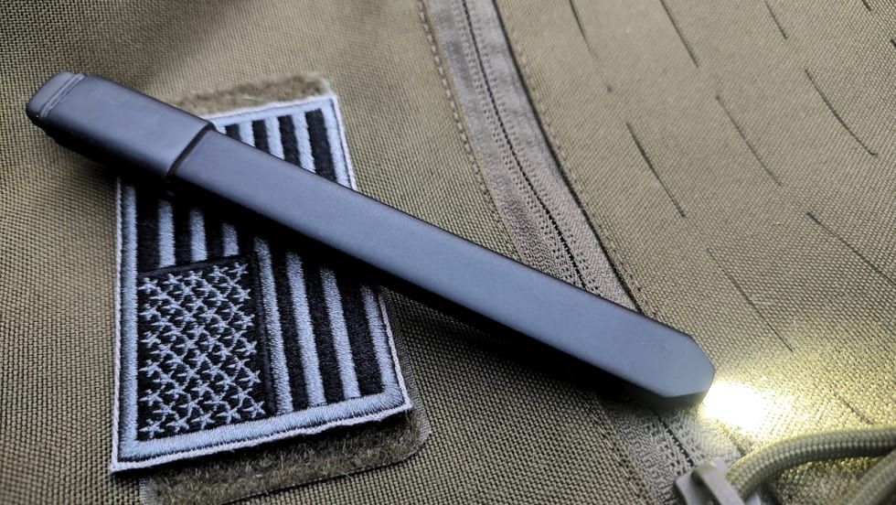 Close-up of a slim black Streamlight Wedge SL flashlight resting on an olive tactical vest with a black-and-gray American flag patch, its LED illuminated to showcase the compact everyday carry design.
