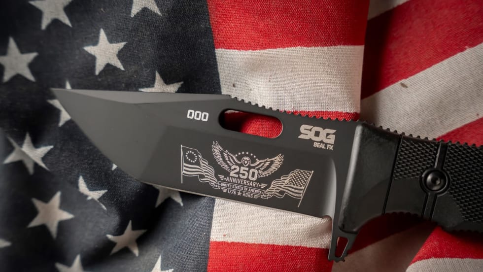 Close-up of a black SOG Seal FX knife featuring a commemorative 250th anniversary engraving on the blade, displayed on an American flag to honor the United States' semiquincentennial.
