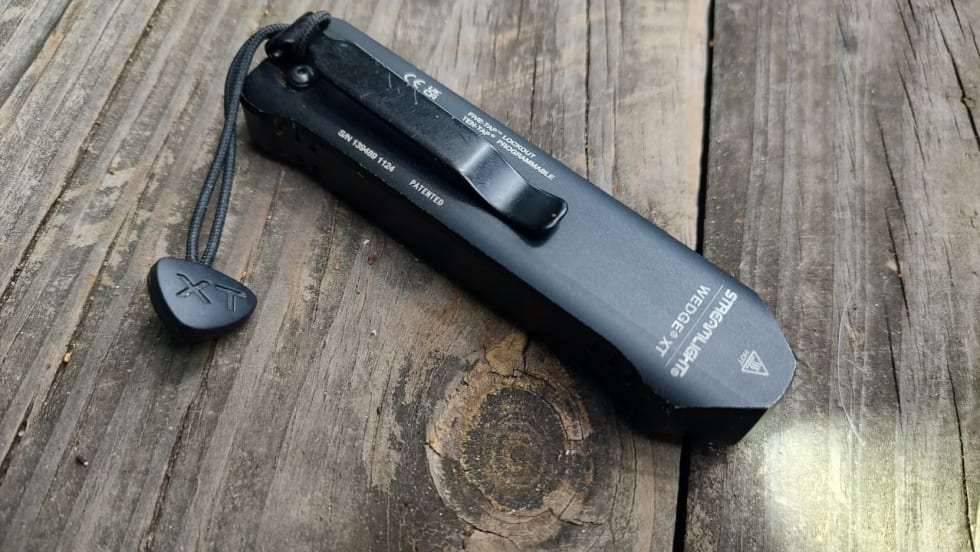 Streamlight Wedge XT compact rechargeable EDC flashlight with pocket clip and wrist lanyard rests on a weathered wooden tabletop, highlighting its slim profile and rugged design.