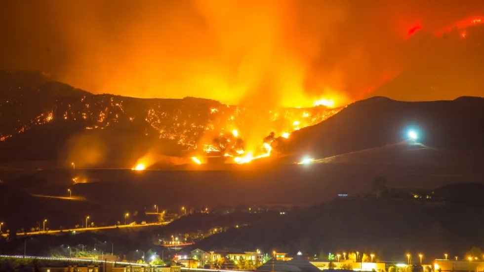 Wildfire burning across hills at night with flames and smoke lighting the sky