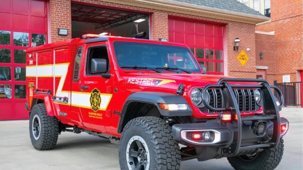Red Morgan Olson Kestrel fire response truck parked outside a fire station, featuring off-road tires, emergency lights, and equipment compartments for first responder use.