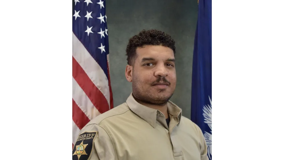 Sheriff's deputy in tan uniform posing with American and state flags