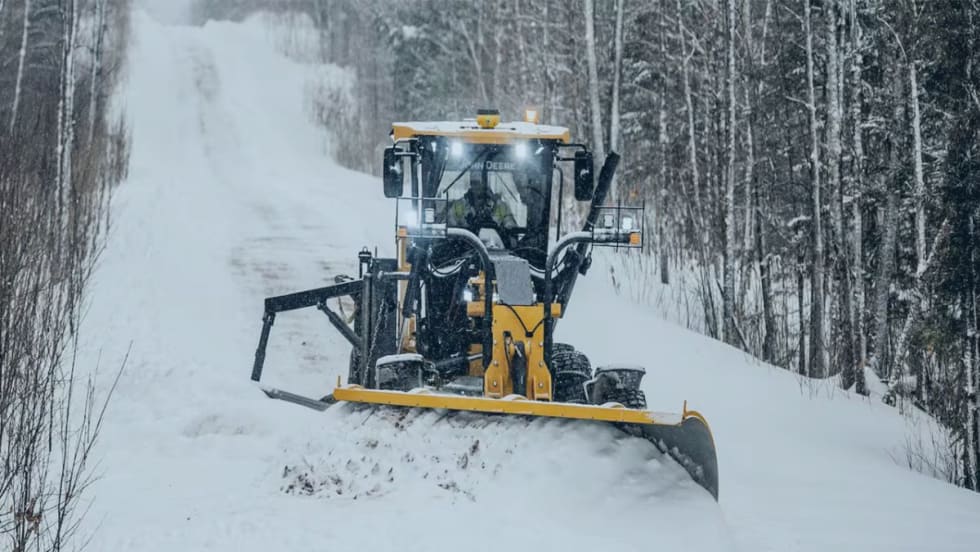 A John Deere plow is clearing snow in a road.