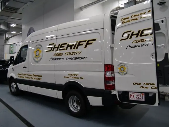 A white electric cargo van is shown with the Cobb County Sheriff's Office logo and badge on the sides.