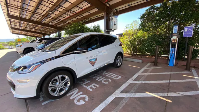 A white Chevy Bolt with a city decal sits in a covered EV parking space.