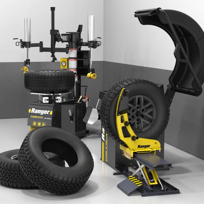 Ranger wheel lift and tire changer equipment displayed in an automotive service bay with off-road tires and shop tools.