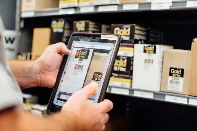 A man holding a tablet while taking a photo of packages.