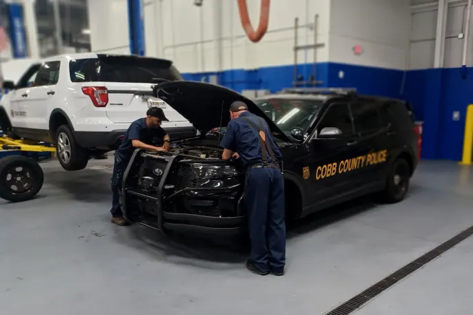 Two technicians work under the hood of a black Ford Police Interceptor Utility for the Cobb County Police Department.