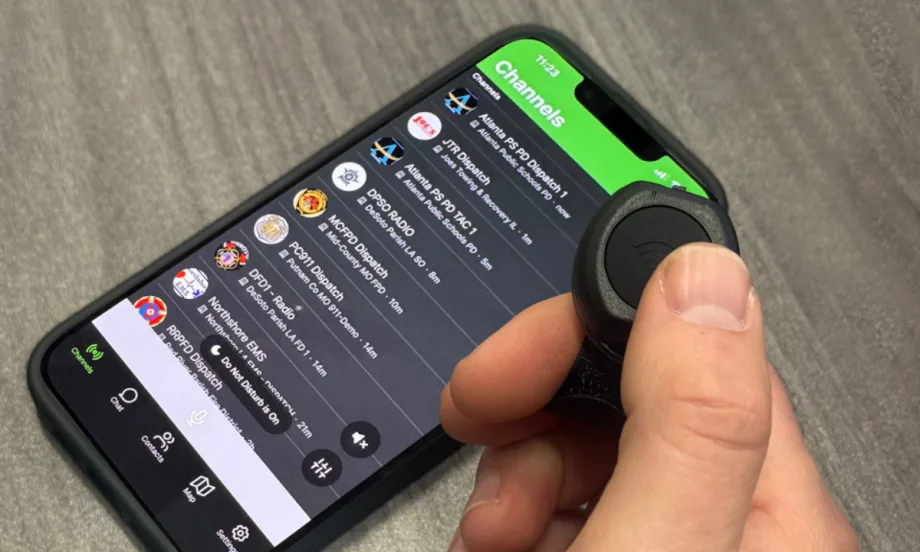 Closeup photo of man's hand using a thumg to push a push to talk button with phone on table.