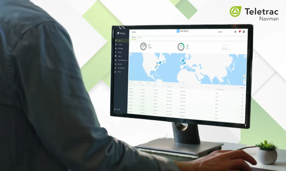 Person using Teletrac Navman’s TN360 fleet management platform on a desktop monitor displaying a world map and vehicle data, with the Teletrac Navman logo on a light background.