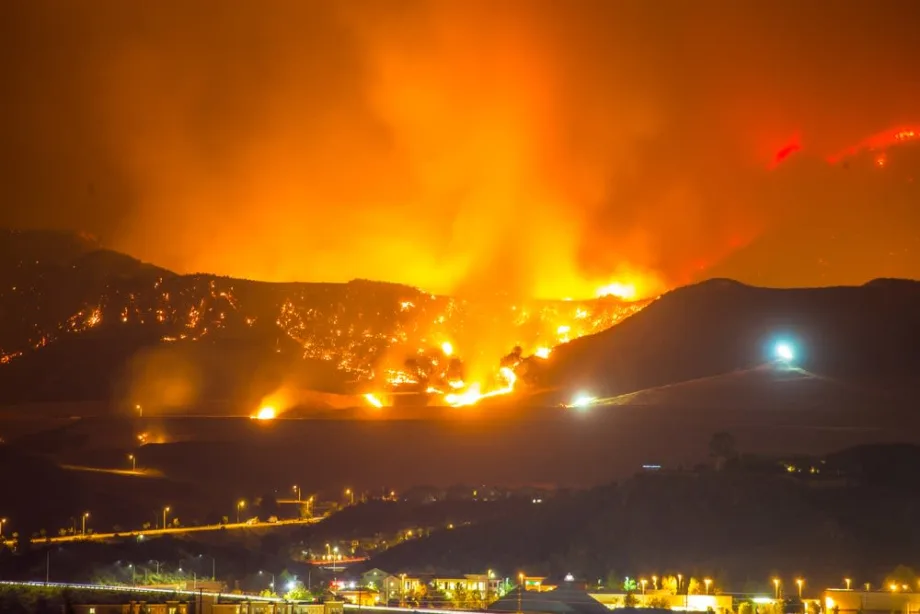 Wildfire burning across hills at night with flames and smoke lighting the sky