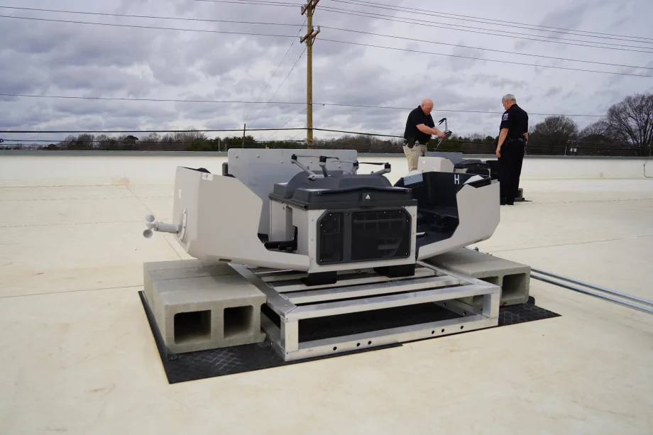 Two police officers stand near a rooftop drone launch system, preparing equipment for a first responder program providing aerial support to emergency calls.