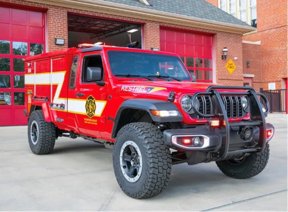 Red Morgan Olson Kestrel fire response truck parked outside a fire station, featuring off-road tires, emergency lights, and equipment compartments for first responder use.