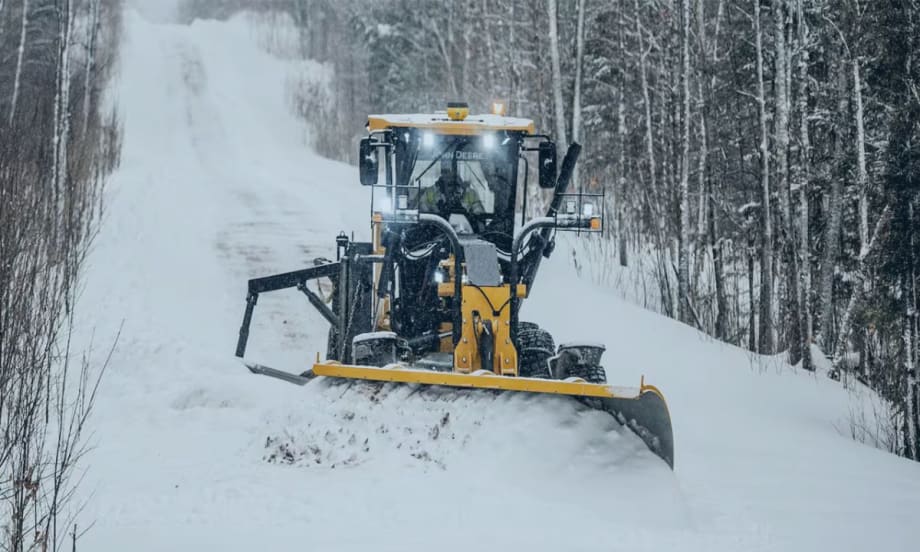 A John Deere plow is clearing snow in a road.