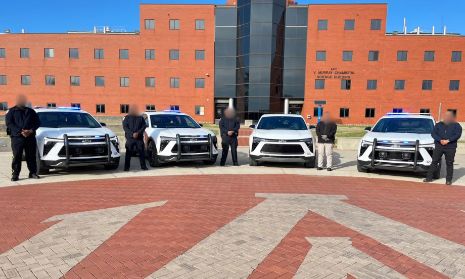 Five Alabama A&M police officers pose with four electric patrol SUVs on campus in front of a brick academic building.